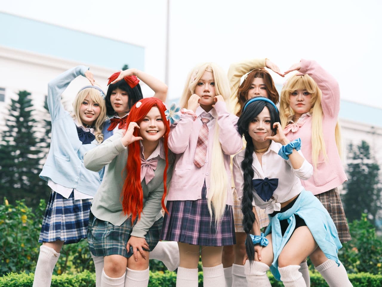 Seven people in coordinated pastel school-uniform styling posing outdoors in a group lineup.