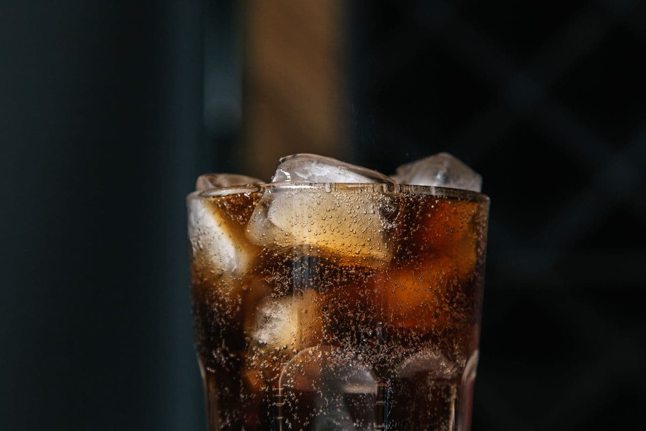 Close-up of a fizzing glass of cola with ice cubes and condensation.