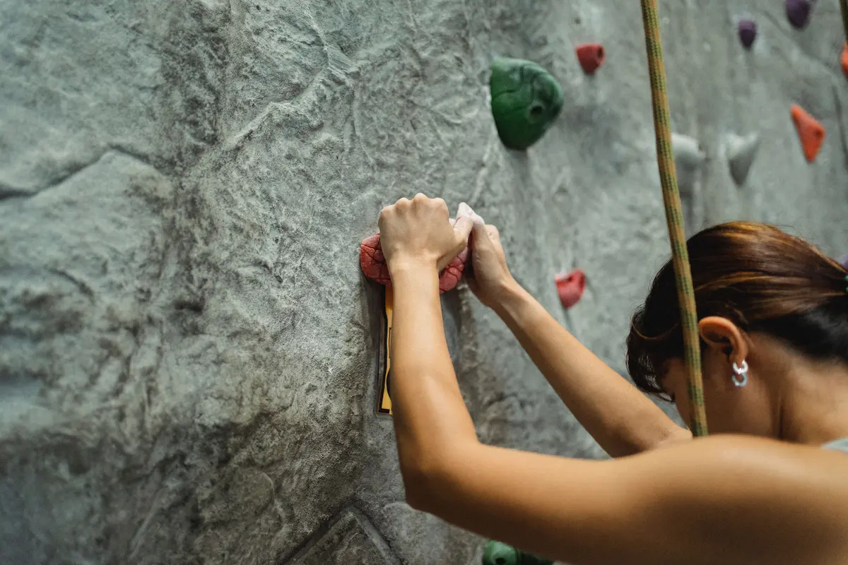Woman rock climbing, relying on pure grip strength to hold onto the wall