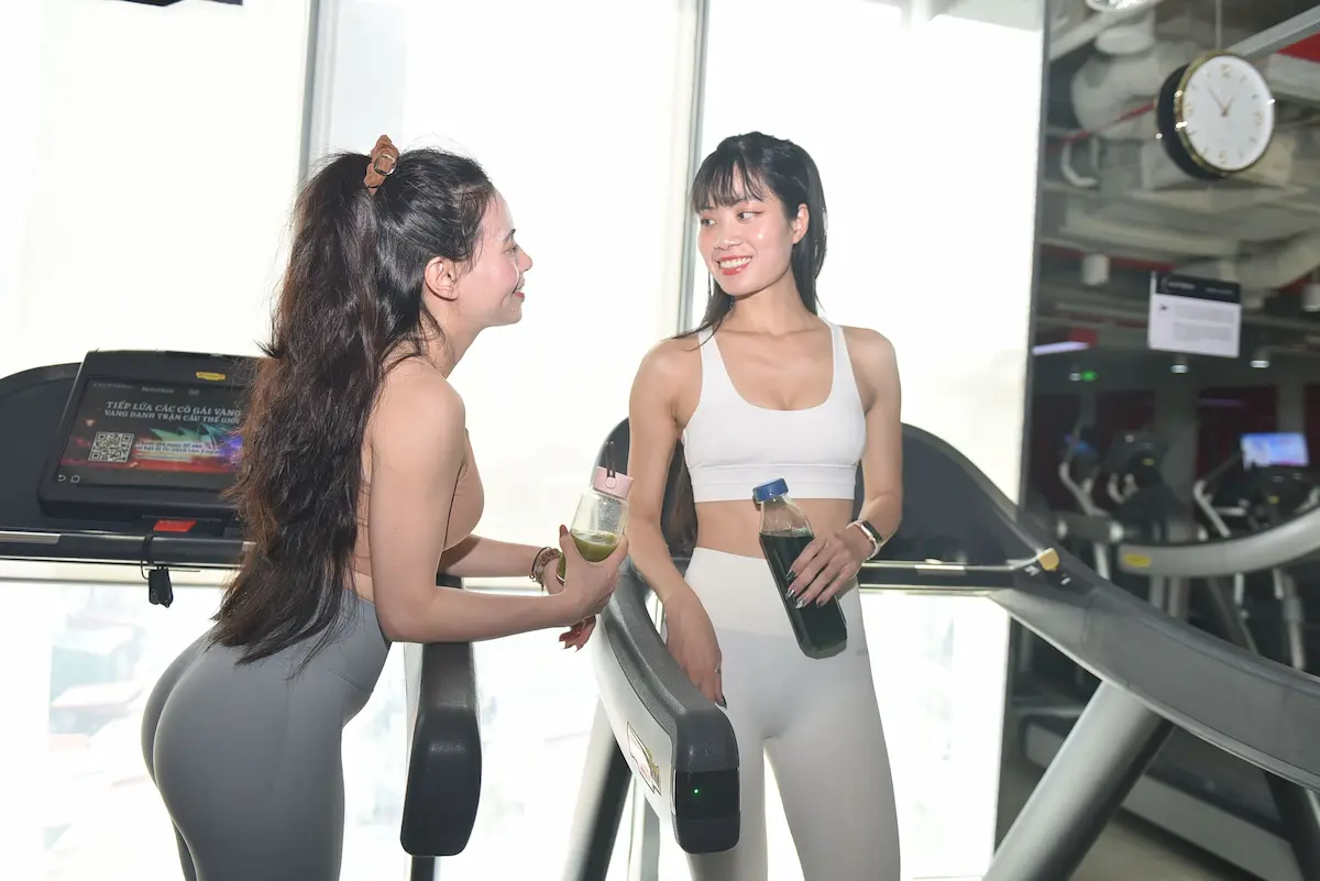 Two women chatting and smiling on treadmills at the gym